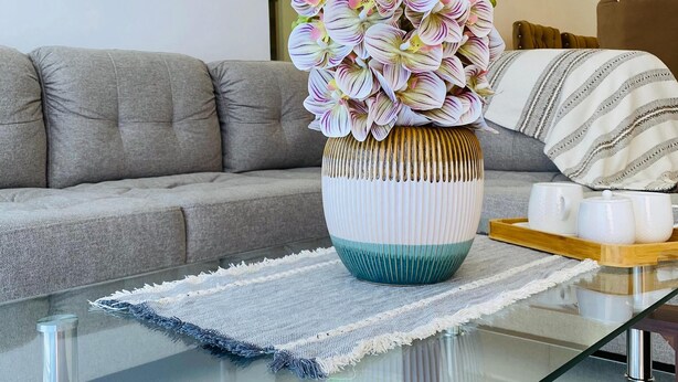 Una sala moderna con una mesa de centro de vidrio, un sofá gris y un florero decorativo con flores.