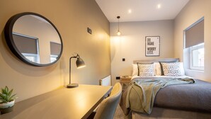 Ein Schlafzimmer mit Bett, Nachttisch, Lampe und einem motivierenden Zitat an der Wand.