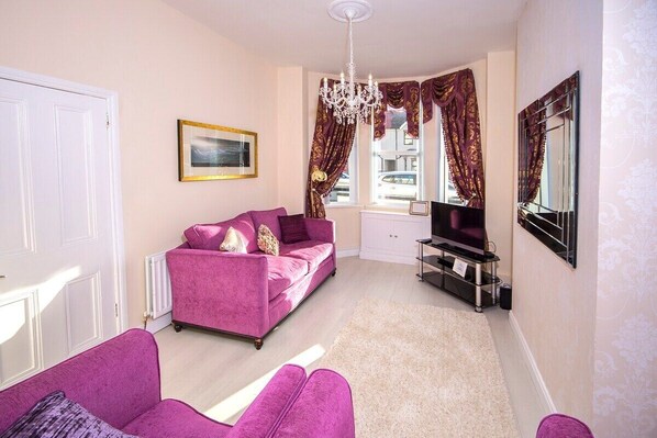 A living room with a pink sofa, a television, and a chandelier.