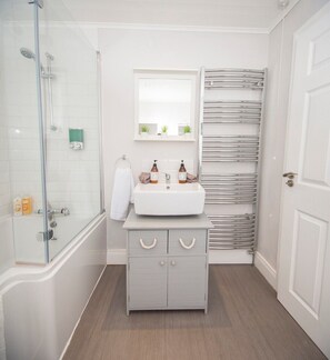 A bathroom with a glass shower enclosure, a white sink with two bottles, a mirror above the sink, and a towel rack.