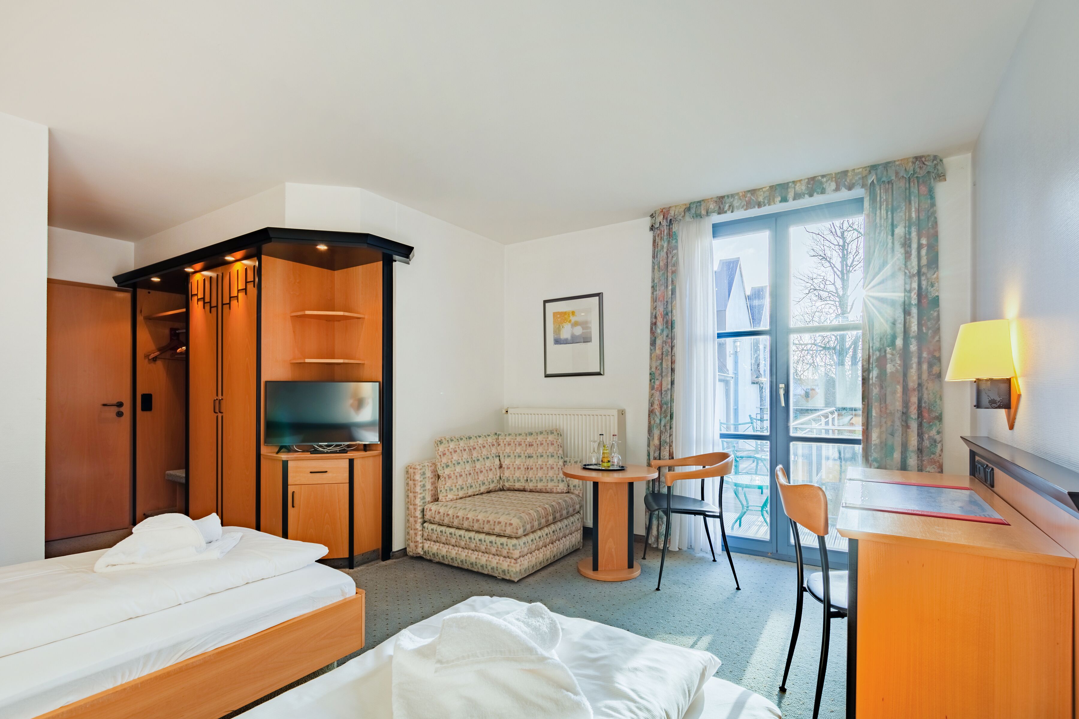 Une chambre d’hôtel avec un lit, un petit canapé, un bureau avec une chaise, une télévision et une fenêtre avec des rideaux.