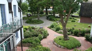 A courtyard with a winding brick pathway, surrounded by lush greenery and trees. - Hotel Rügenschmiede vis a vis Hiddensee (Schaprode)