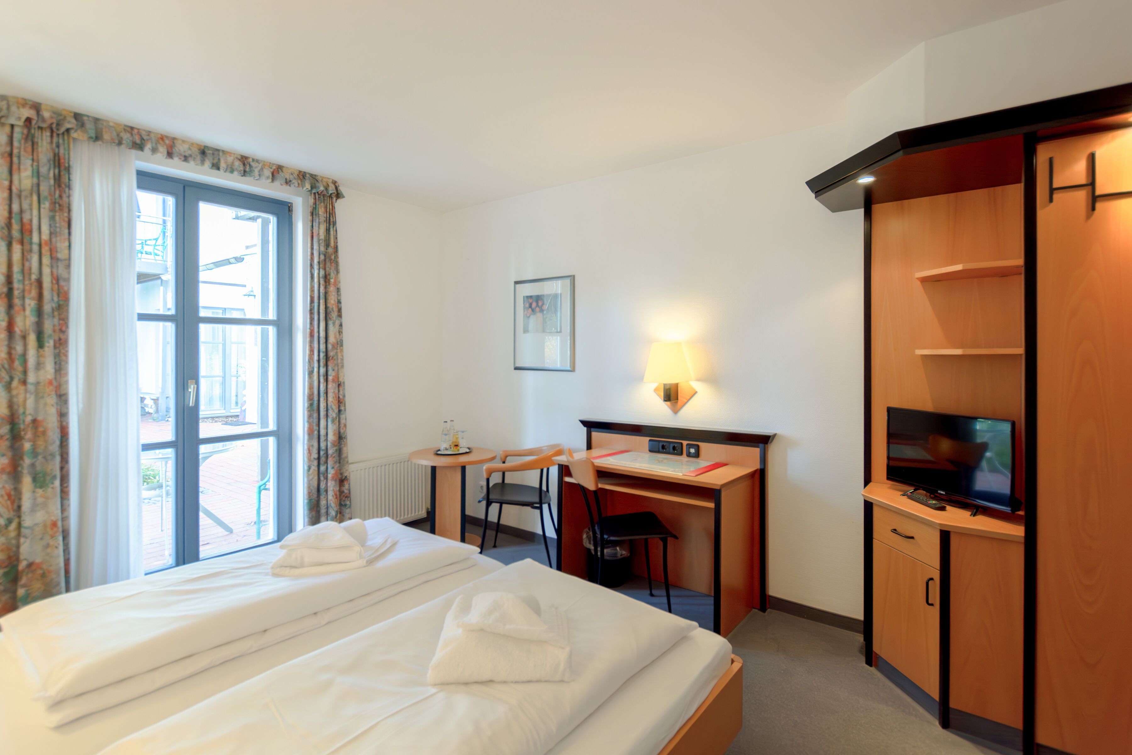 A hotel room with a bed, desk, chair, TV, and a window with curtains.