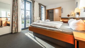 A modern hotel room with a large bed, a wooden headboard, a bathroom with a shower, and a view through the window. - Hotel Rügenschmiede vis a vis Hiddensee (Schaprode)