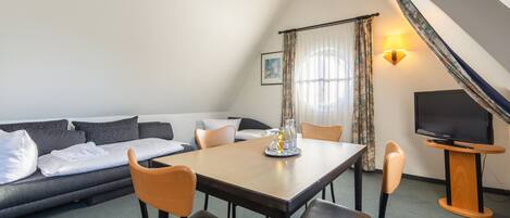A modern room with a sofa, dining table, chairs, a TV, and a lamp.
