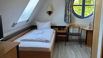 Un dormitorio con tragaluz, una cama, un escritorio, una silla y una ventana con vista a árboles.