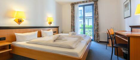 Habitación de hotel con cama doble, dos lámparas de noche, un escritorio con silla y vistas al exterior a través de una ventana con cortinas.