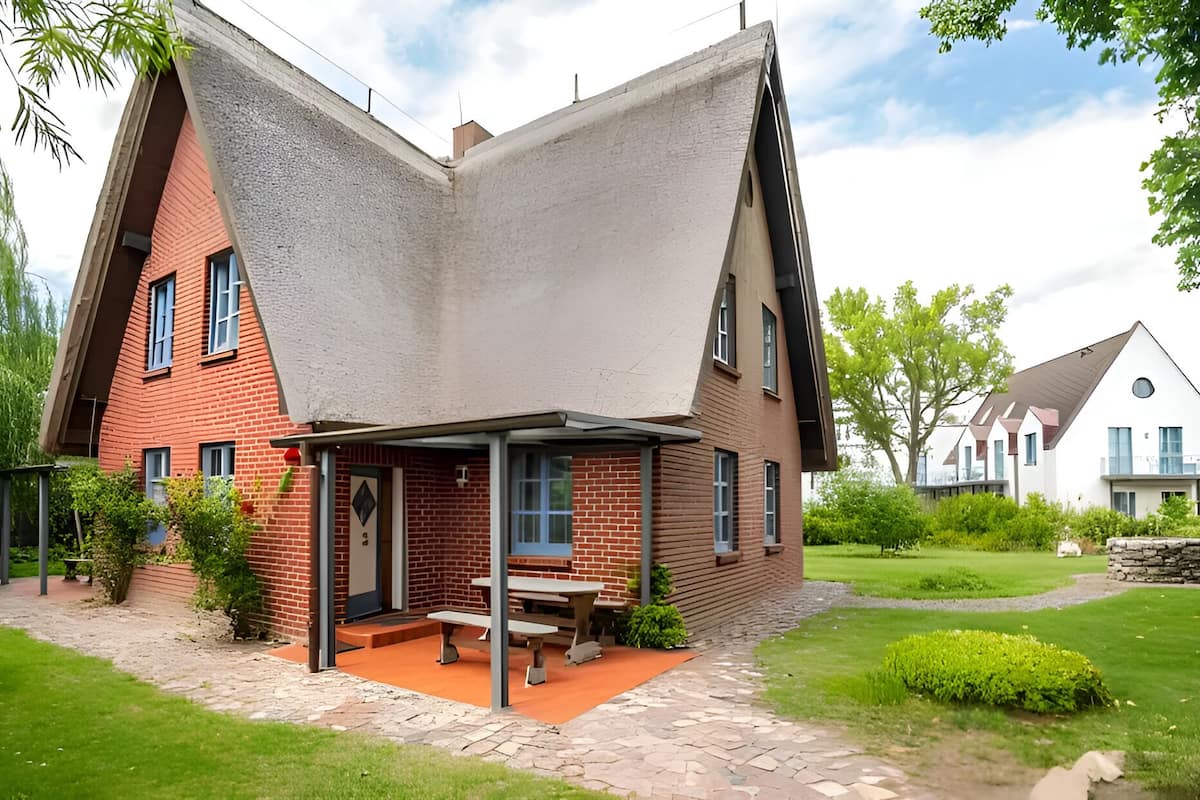 A modern house with a sloped roof, a patio with a table and benches, and a well-maintained garden.