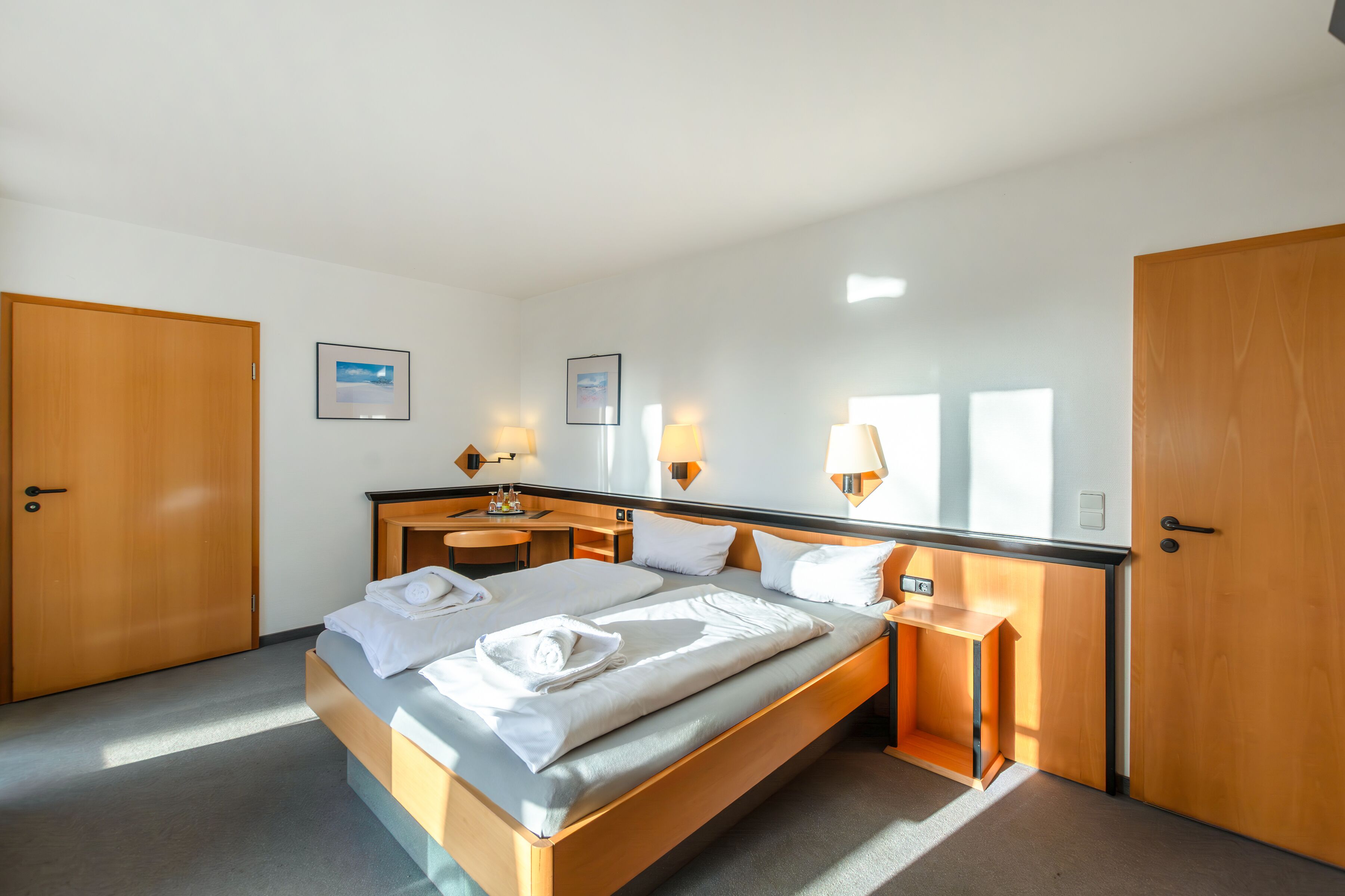 A hotel room with a large bed, wooden wardrobe, bedside tables, and wall-mounted lamps.