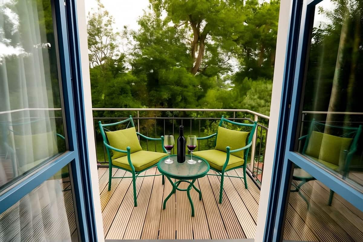 A balcony with two green chairs and a small table, surrounded by glass railings.