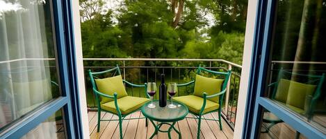 A balcony with two green chairs and a small table, surrounded by glass railings.