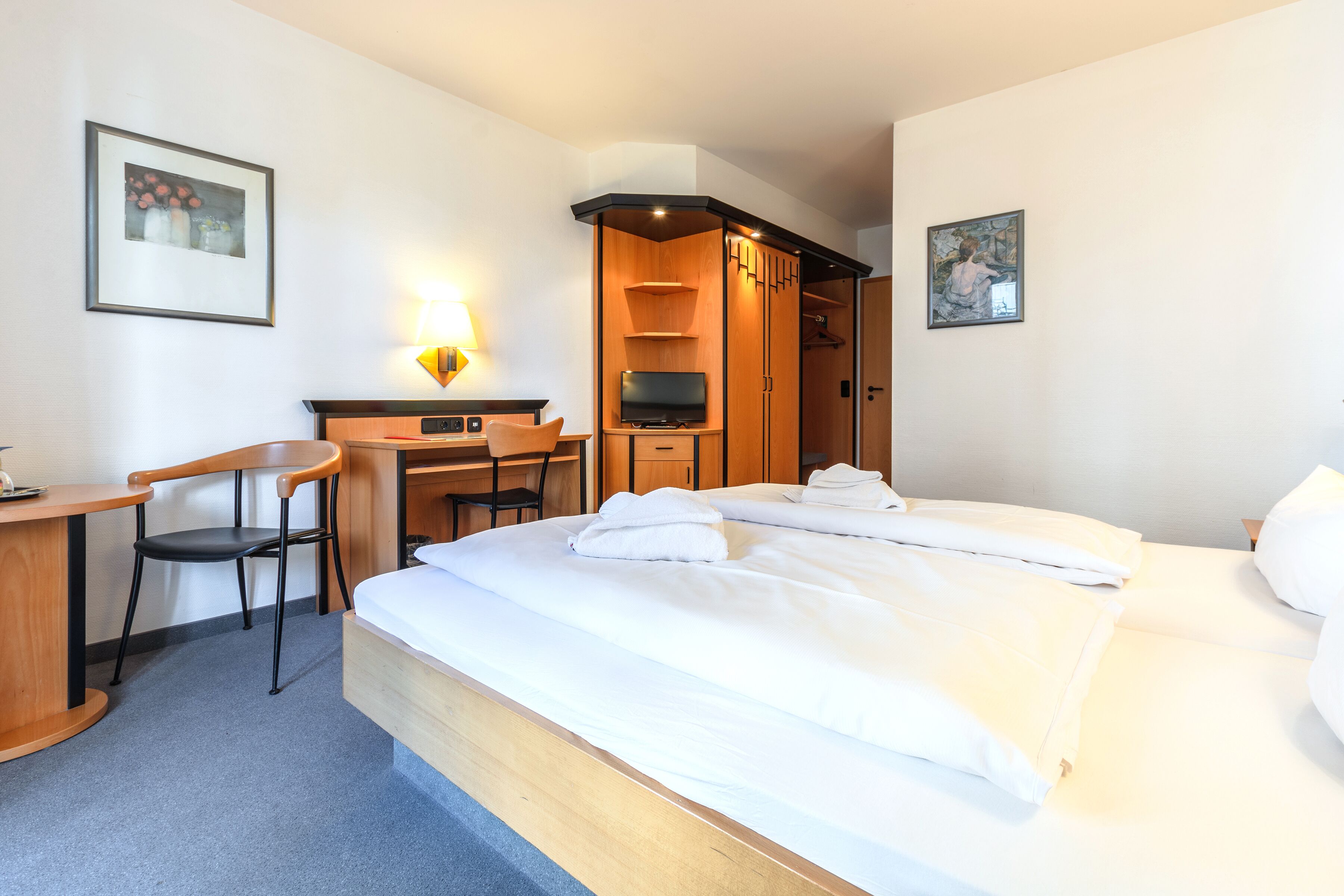 Een hotelkamer met een bed, een bureau met stoel, een televisie en een kledingkast.