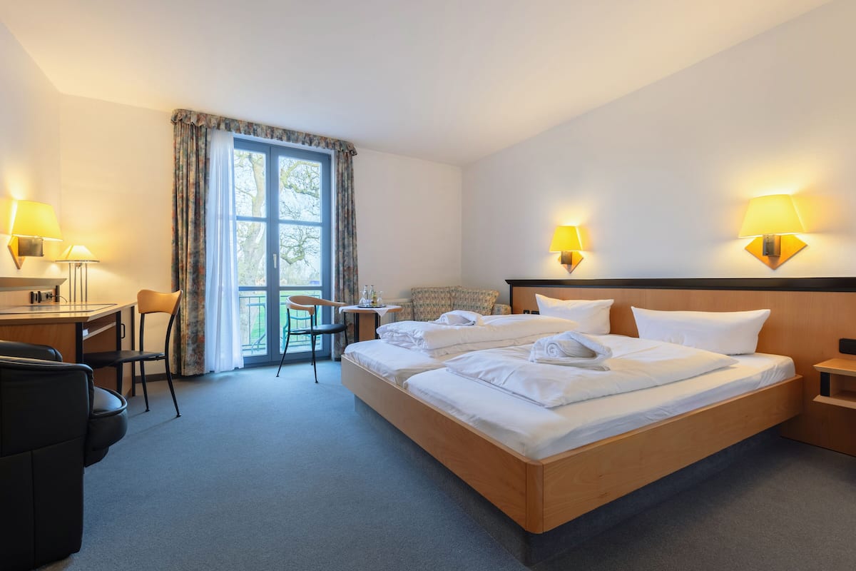 A hotel room with a large bed, a desk, a chair, and a small table.