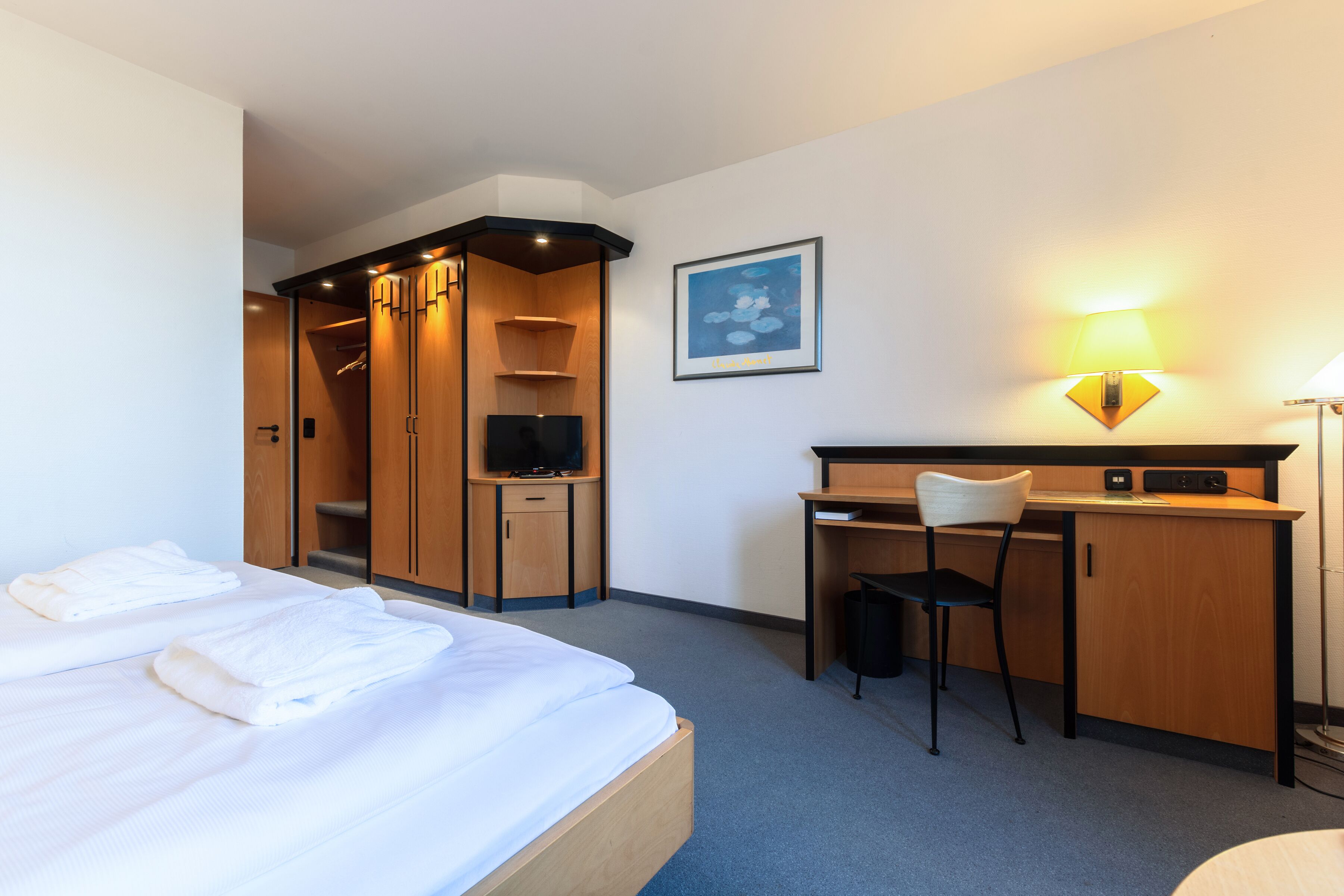 A hotel room with a bed, a desk, a chair, a TV, and a lamp.
