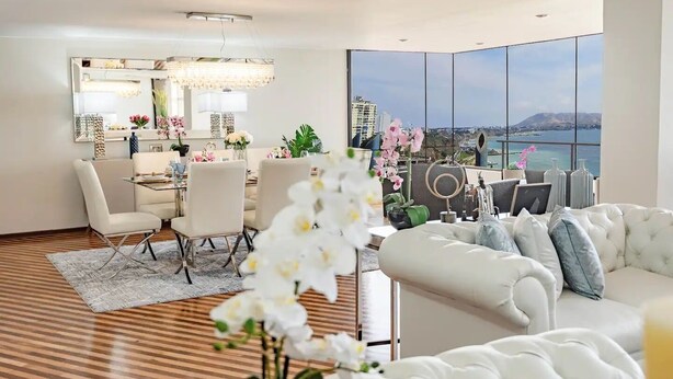 A modern living room with a dining area, large windows with a city view, and a white sofa. - OceanFront Pacific Luxe & Stunning views (Miraflores)