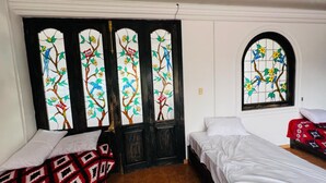 A room with a large stained glass door featuring birds and flowers, two single beds, and a small window with a similar design.