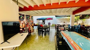 An outdoor dining area with tables and chairs, a TV on a stand, and a colorful mural on the wall.