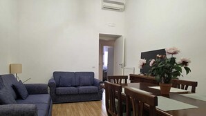 Un salon avec un canapé, une table à manger et des chaises, ainsi qu’une plante en pot.