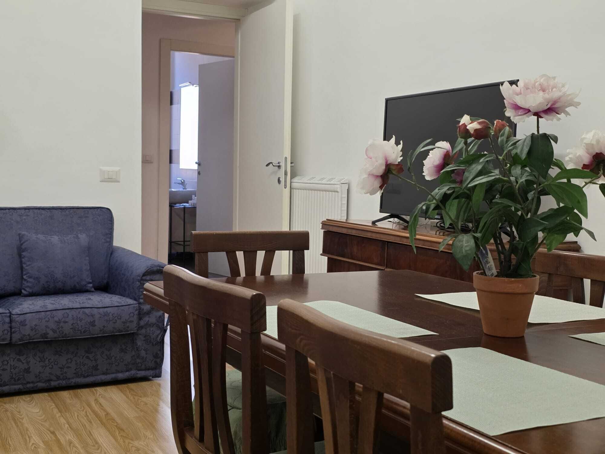 A living room with a blue sofa, wooden dining table, chairs, a potted plant, and a blackboard on the wall.