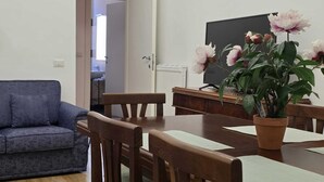 Un salon avec un canapé bleu, une table à manger en bois, des chaises, une plante en pot et un tableau noir accroché au mur.