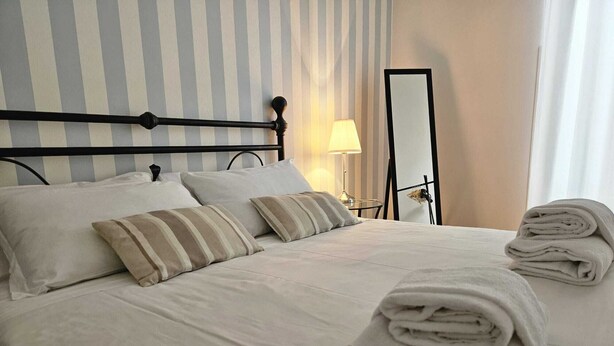 Un lit bien fait, avec des oreillers et des serviettes pliées, une lampe de chevet et un miroir sur un mur à rayures.