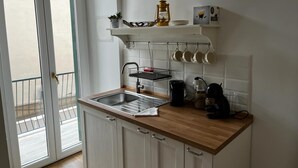 Une petite cuisine équipée d’un évier, d’une machine à café et d’une étagère où sont posées des tasses et une plante.