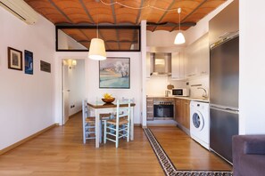 A compact kitchen with a washing machine, a dining area with a table and chairs, and a hallway leading to a bedroom. - Iconic Old Town - Unik Vacation (Tarragona)
