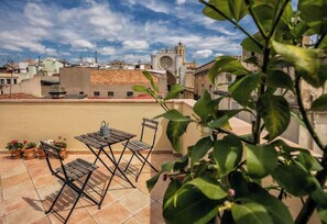 A rooftop terrace with a table and chairs, potted plants, and a view of a historic building with a clock tower. - Iconic Old Town - Unik Vacation (Tarragona)