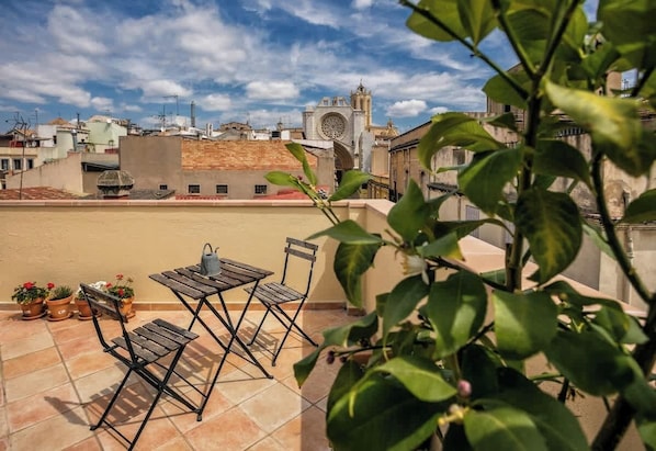 A rooftop terrace with a table and chairs, potted plants, and a view of a historic building with a clock tower.