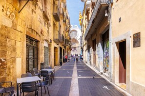 A narrow street with buildings on either side, outdoor seating, and a prominent cathedral in the background. - Iconic Old Town - Unik Vacation (Tarragona)