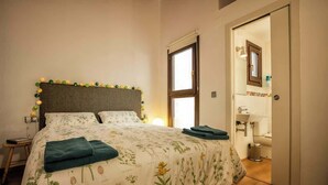 Quarto com cama, mesa de cabeceira e vista para o banheiro.