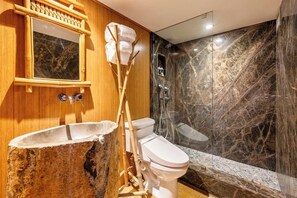Um banheiro com toucador de madeira, vaso sanitário branco, parede de chuveiro em mármore e banheira.