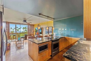Une cuisine moderne dotée d’un grand îlot central, de meubles en bois et offrant une vue sur les palmiers.