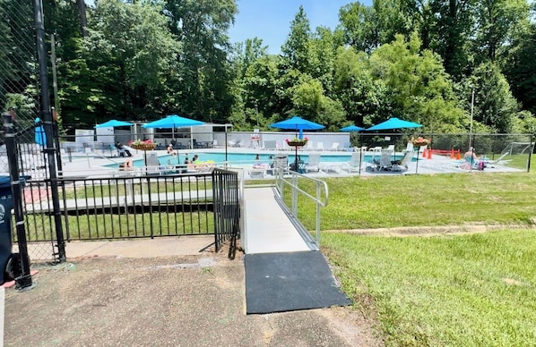 Un espace piscine doté d’une terrasse entourée d’une clôture, de chaises longues et de parasols.