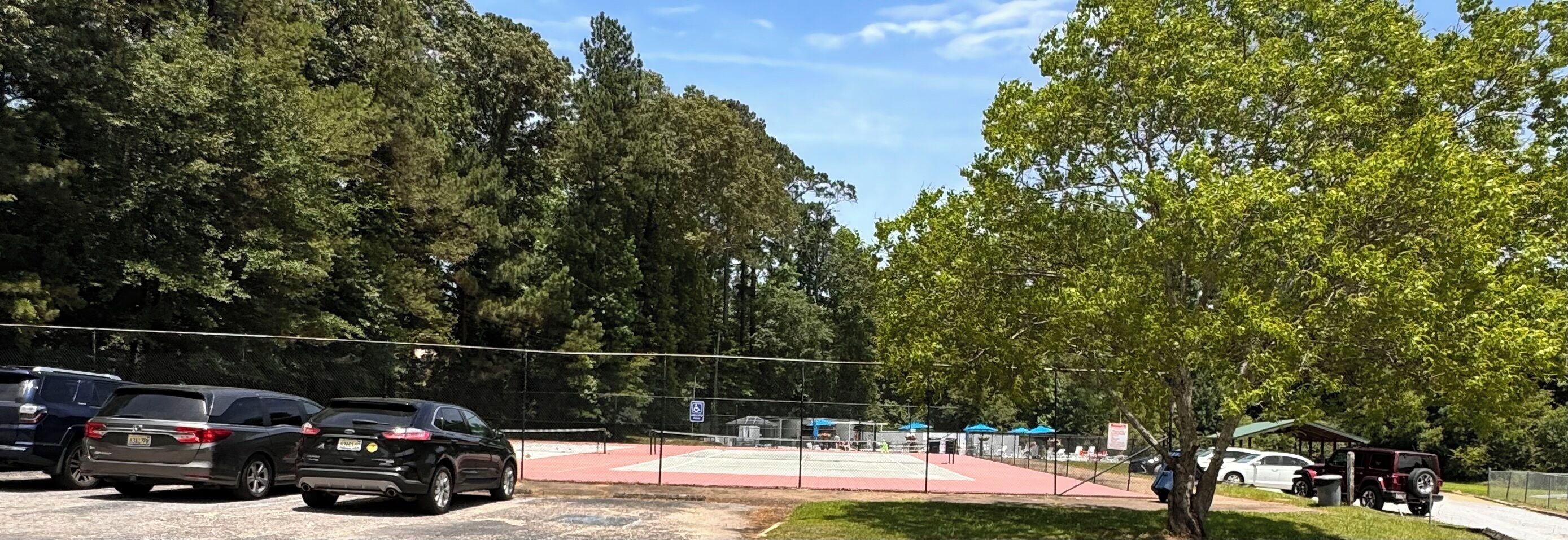 Un espace de stationnement avec plusieurs voitures, un court de tennis et un espace de repos abrité.