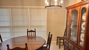 Uma sala de jantar com uma mesa redonda de madeira, seis cadeiras, um lustre e um aparador.