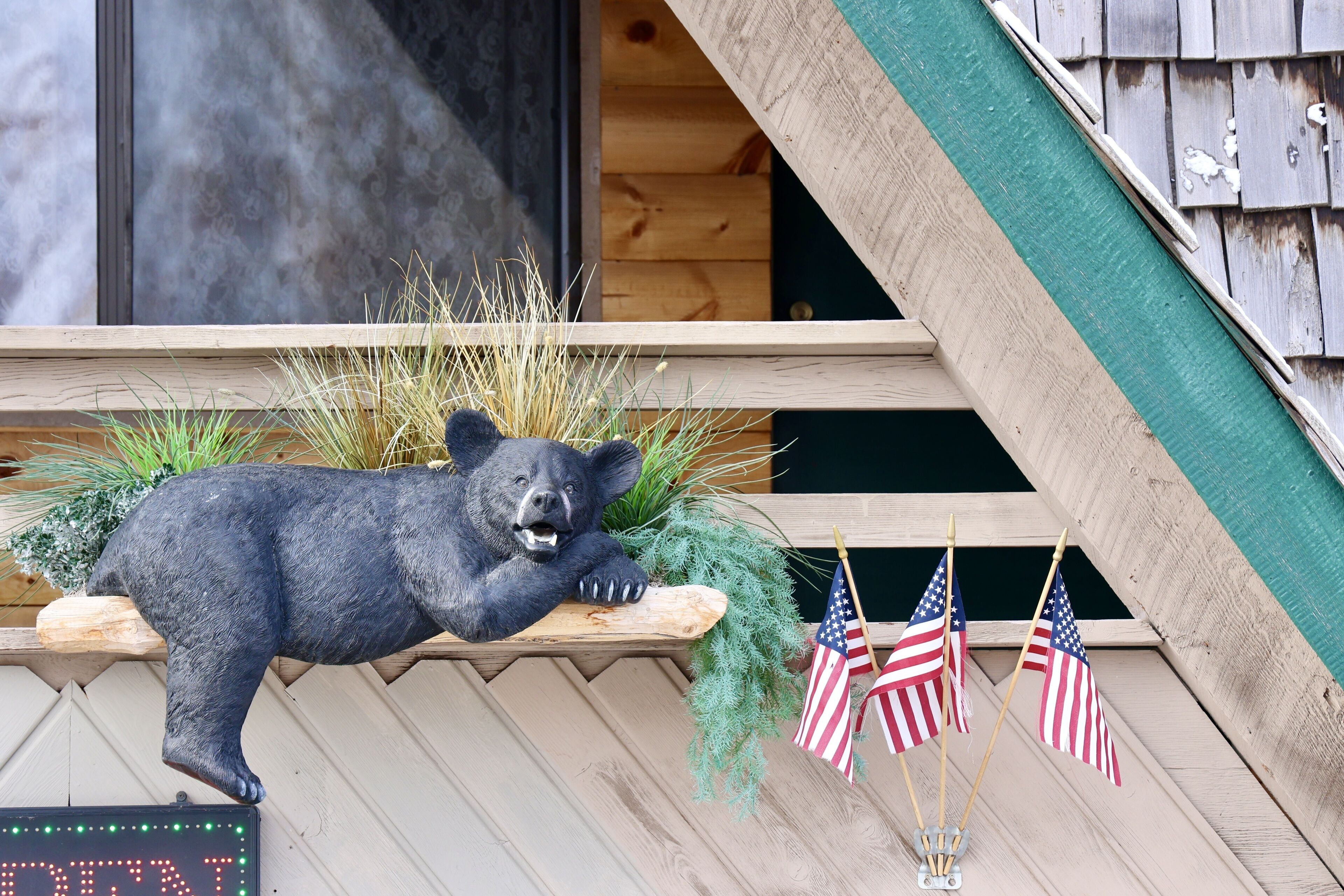 Una estatua de oso sobre un repisa de madera, banderas estadounidenses y un letrero con letras iluminadas.