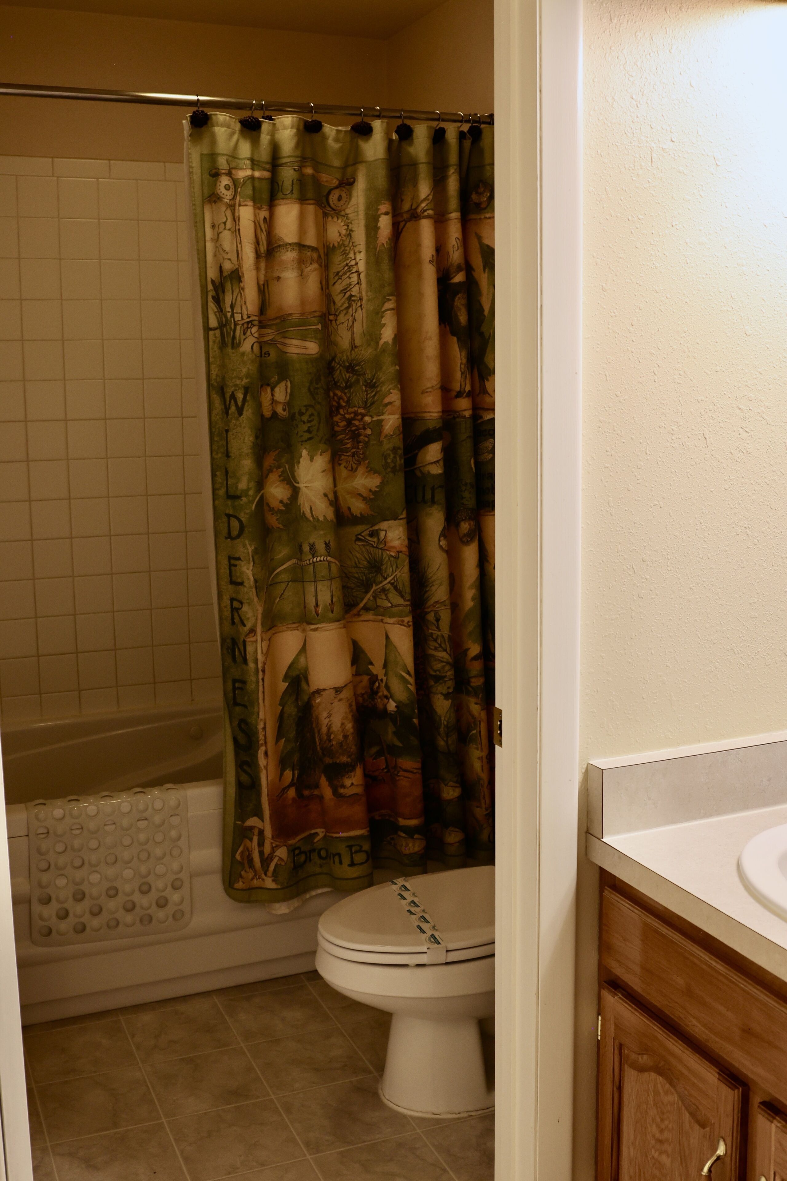A bathroom with a shower curtain featuring a nature design, a toilet, and a bathtub with a built-in seat.