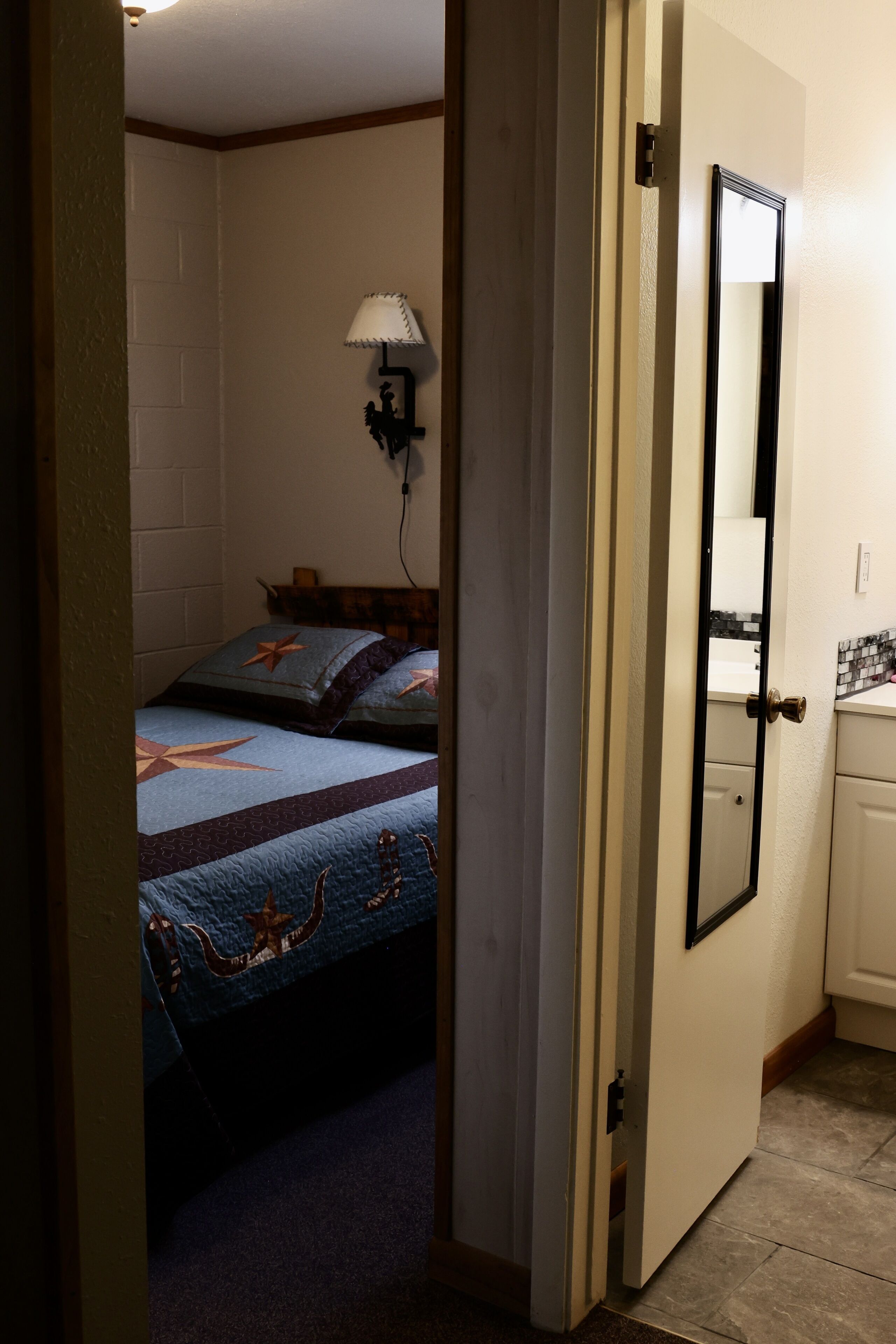 A bedroom with two beds, a nightstand, a lamp, and a bathroom visible through an open door.