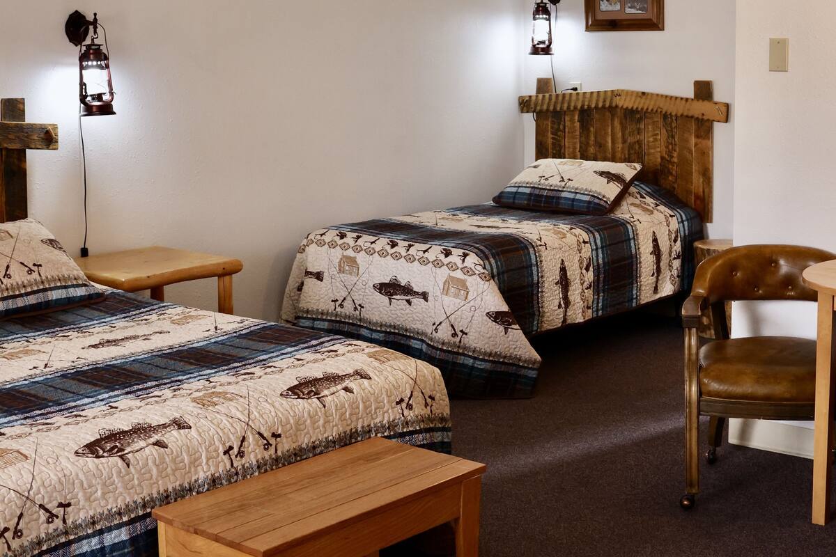Een slaapkamer met twee bedden, een houten bankje, een fauteuil van bruin leer en twee wandlampen.