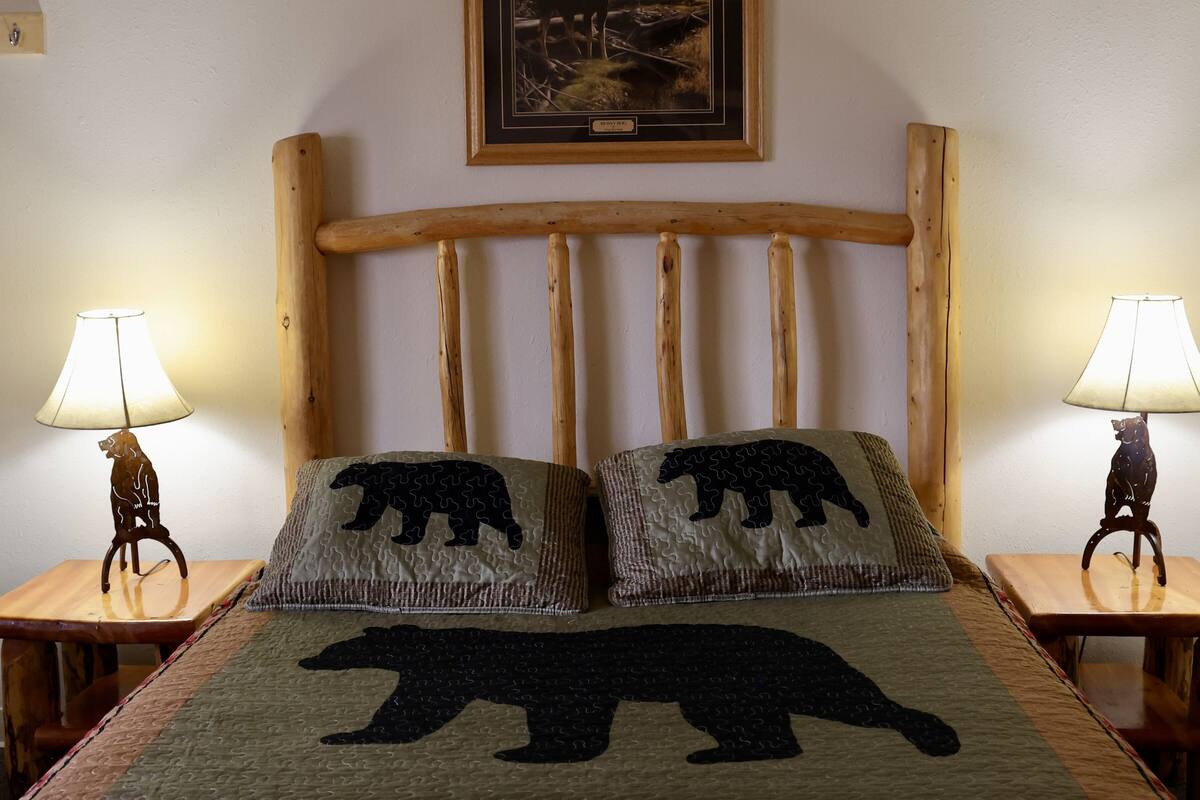 Een bed met een houten hoofdbord, twee nachtkastjes met lampen en twee kussens met berenmotieven.