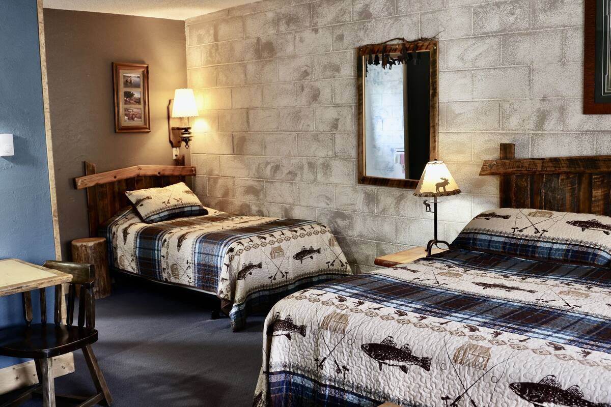 Een kamer met twee bedden, een houten stoel, een klein tafeltje, een lamp en een spiegel tegen een gestructureerde muur.