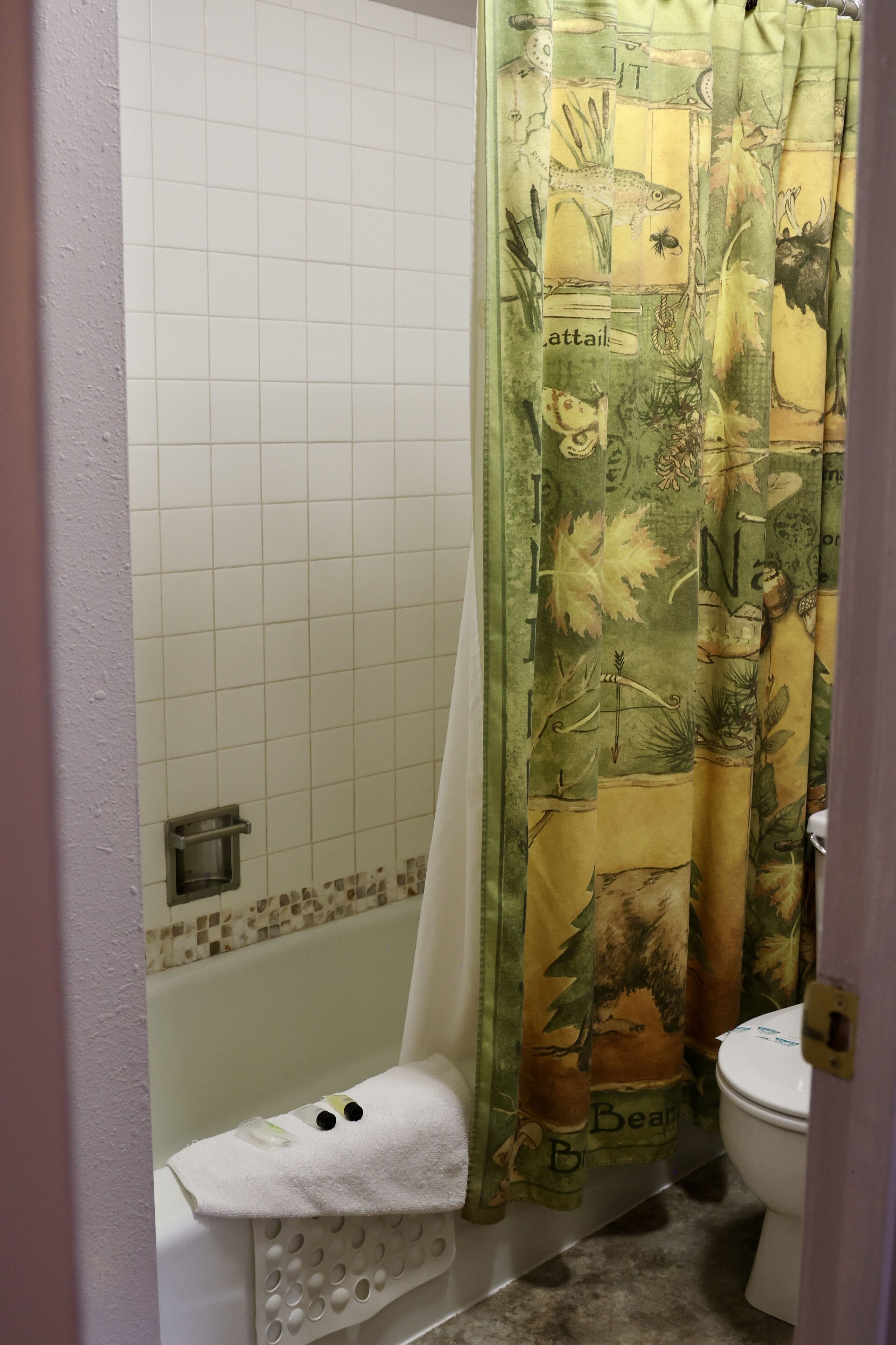 Een badkamer met douchegordijn met natuurprint, een witte badkuip en een toilet.