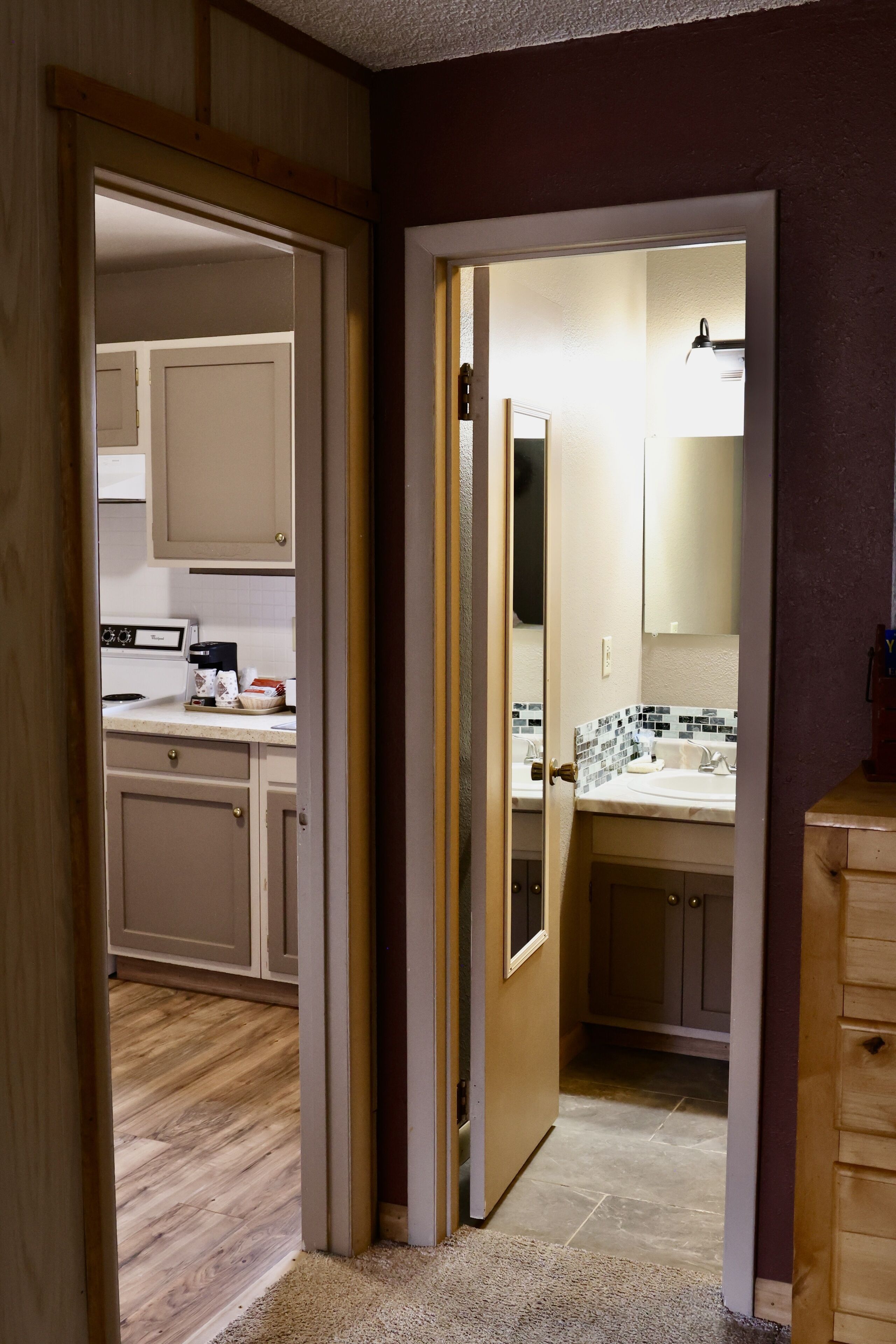 A hallway leading to a kitchen and a bathroom with a tiled backsplash.