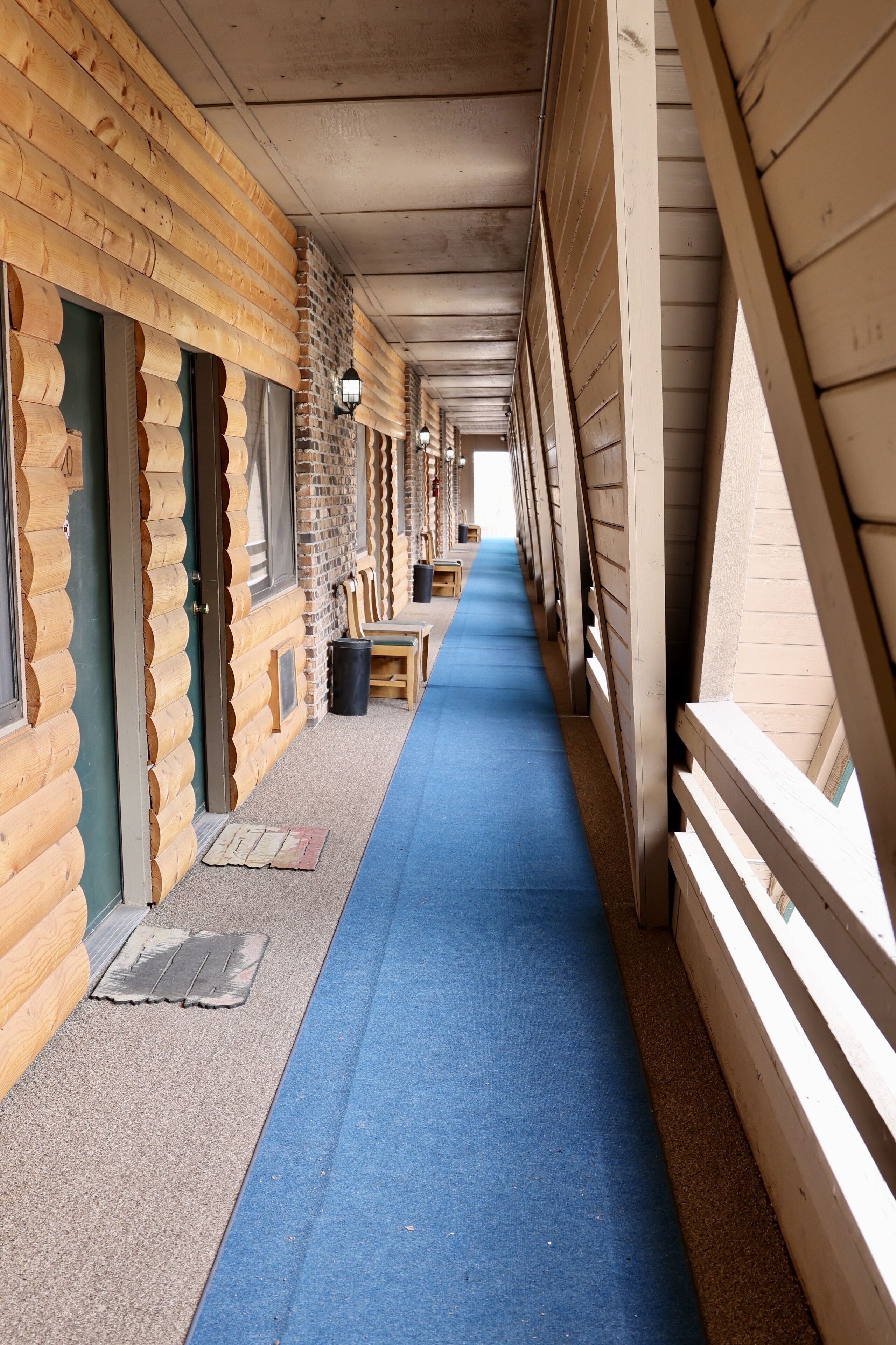 Un couloir aux murs en bois et au tapis bleu, qui mène à une pièce dotée d’une fenêtre et d’une porte.