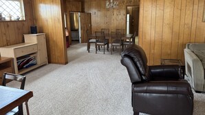 A room with wooden paneling, a dining area with chairs and a table, a leather armchair, and a grey sofa. - Walk to the Mercantile, downtown, Osage Nation offices, Osage Tribal Museum! (Pawhuska)
