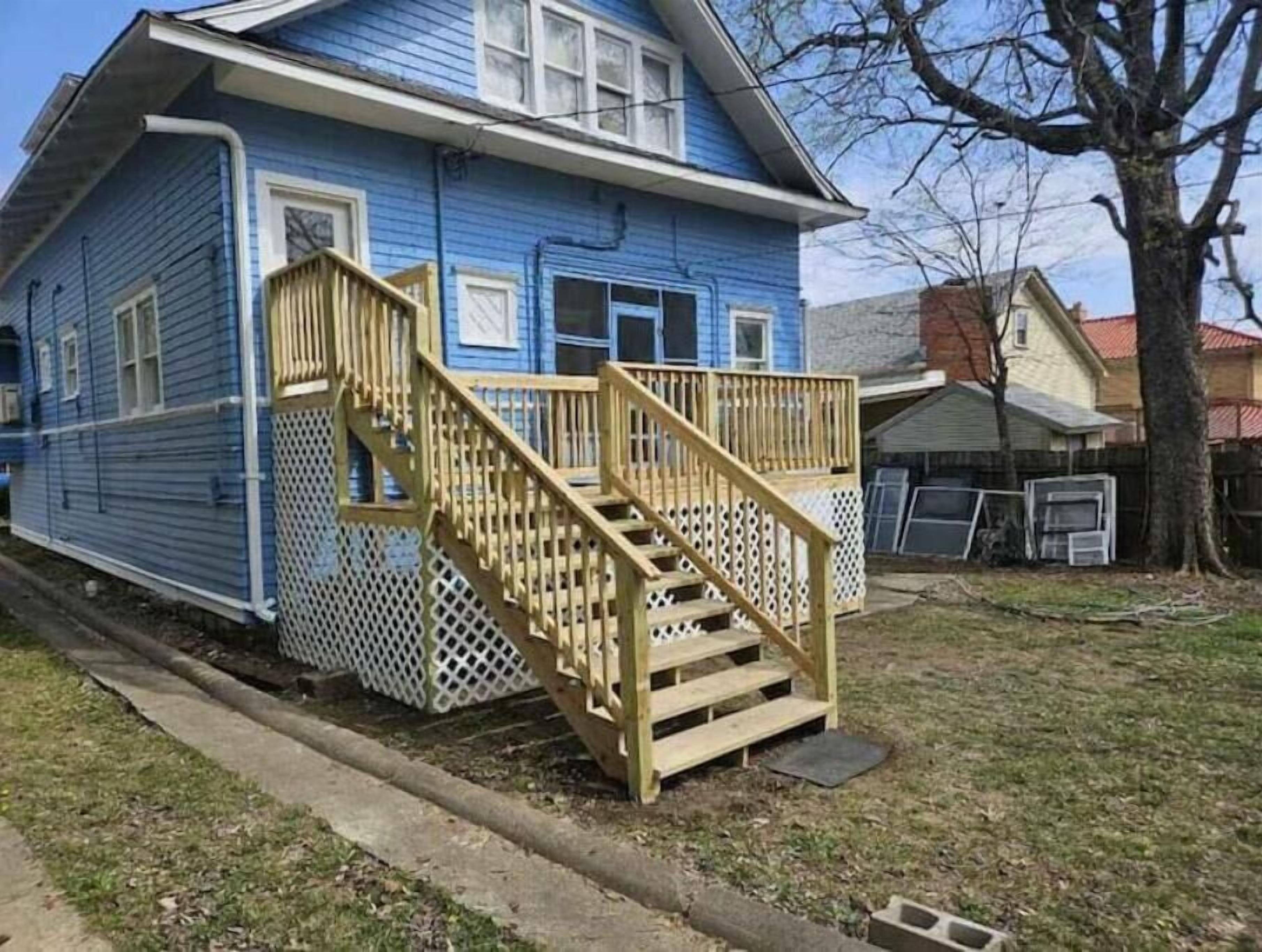 Una casa de dos pisos con una escalera de madera que sube a un porche.