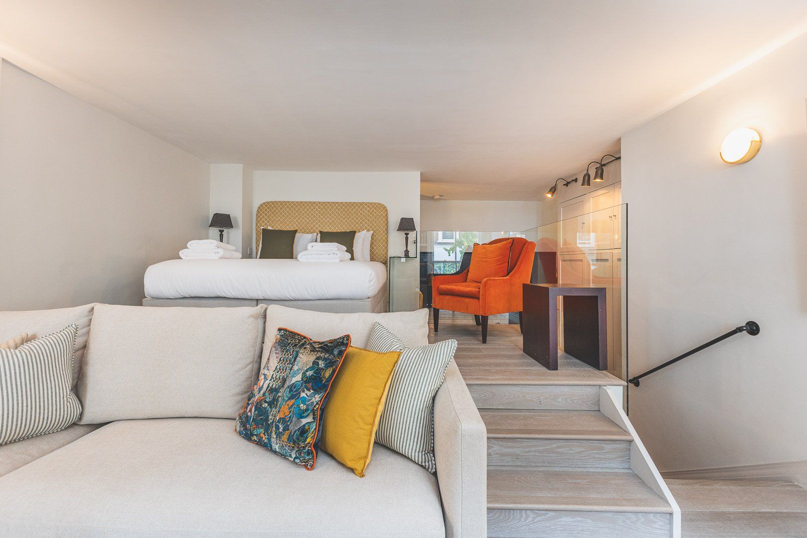 Habitación de hotel con sofá, una silla, cama y escalera que conduce a una zona de cocina.
