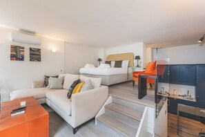 A modern hotel room with a sofa, a bed, a glass table, and a kitchen area.