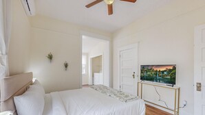 Een slaapkamer met een bed, een plafondventilator, een televisie op een standaard en een deur.